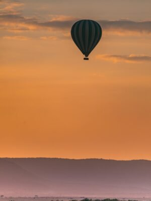 Hot air balloon flying above highlands with orange sunsets and wild animals